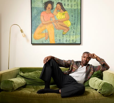 He sits on a green velvet sofa beneath an artwork showing two black women holding hands