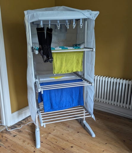 A multi-tier electric clothes airer with a cover holds socks, towels and a blue cloth drying indoors