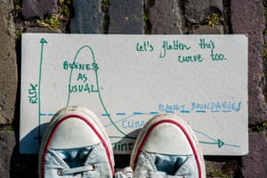 A climate placard saying 'Let's flatten this curve too' is placed on the ground under a pair of trainers