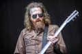 Brett Hinds, with long hair and sunglasses holding a guitar
