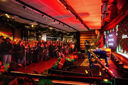 Partridge plays keyboard on stage surrounded by Christmas presents to an audience of schoolchildren and parents