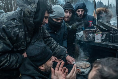 asylum seekers huddle around a stove used to heat food and water