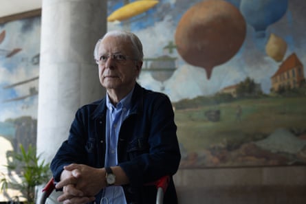 Frei Betto sitting in a building with large mural on the wall behind him.