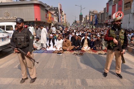 Two officers stand in front of a crowd of Muslim worshippers praying on a road.