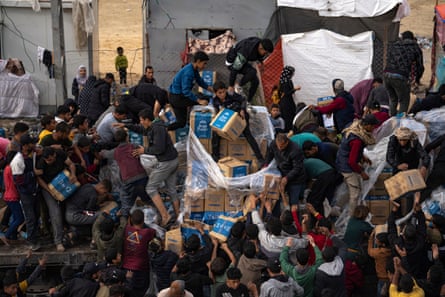 A crowd of men and boys take boxes labelled Aqua Purity from a truck