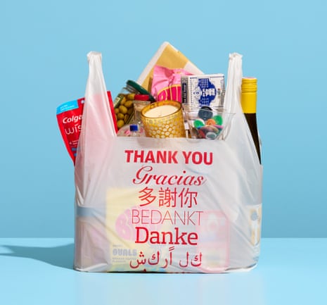 A white plastic shopping bag saying thank you in various languages in red print, containing a scented candle, a bottle, Colgate wisps toothbrushes, olives, etc.