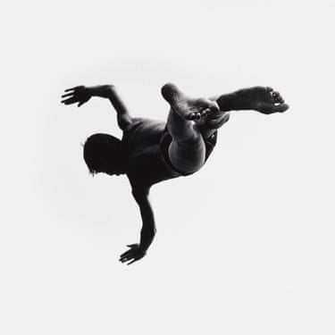 Person performing a backflip, photographed from below in black and white.