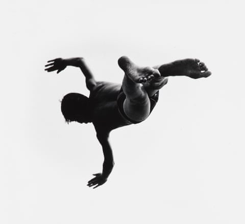 Person performing a backflip, photographed from below in black and white.