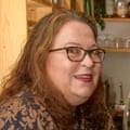 Wendy, with long red wavy hair, glasses and red lipstick, wearing a brown and black patterned dress