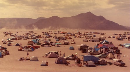 People camp in a barren stretch of dusty land with a mountain in the background.
