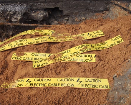 yellow tape signs warning of buried electric cable below in a trench being excavated during roadwork and building construction
