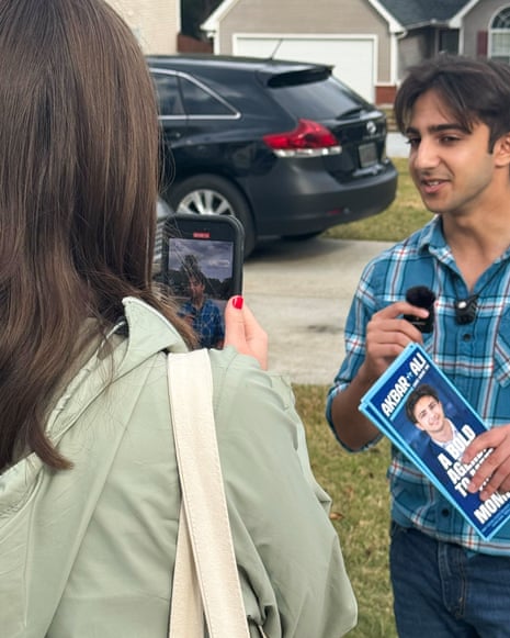 a man speaking in a microphone holding a pamphlet as someone records him