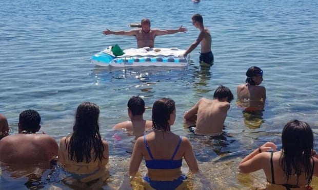 Shirtless priest with inflatable holding mass in sea with young people in bathing suits