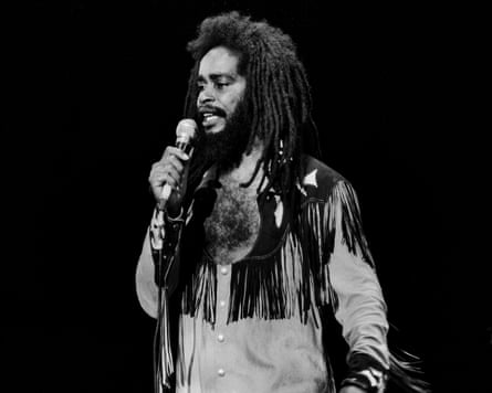 A black and white photo of Max Romeo singing into a microphone with long black dreadlocks