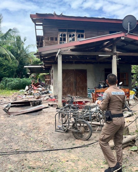 A traffic police officer studies a damaged two-storey house with fallen walls and blown-out windows