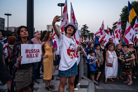 A woman takes a selfie at a march in Tbilisi; another holds a sign that reads ‘Russia Kills!’