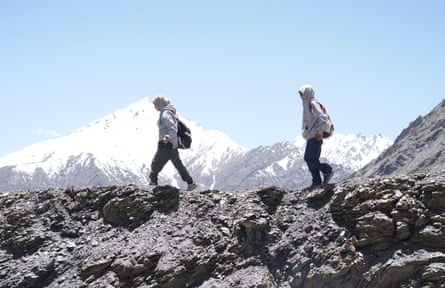 Two young women wearing hijabs on a trail with snow-capped mountains in the distance.