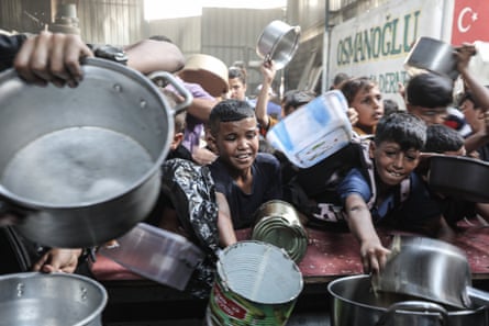 Palestinians, including children, wait with pots to receive hot meals distributed by charity organizations