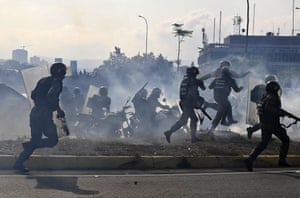 Members of the Bolivarian National Guard loyal to Nicolás Maduro run under a cloud of tear gas after being repelled by guards supporting Juan Guaido