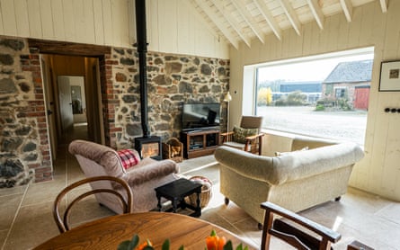 The spacious sitting room at Stable One, with a high ceiling and exposed stonework with a window looking on to a yard.