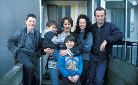 A man and woman and four children standing on the walkway of a block of flats