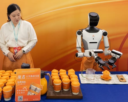 A woman stands beside a robot as it prepares tea