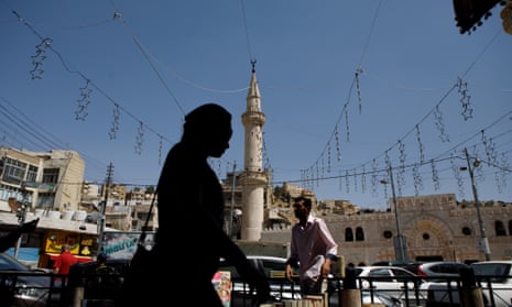 A woman passes a street vendor and a minaret in Amman, Jordan