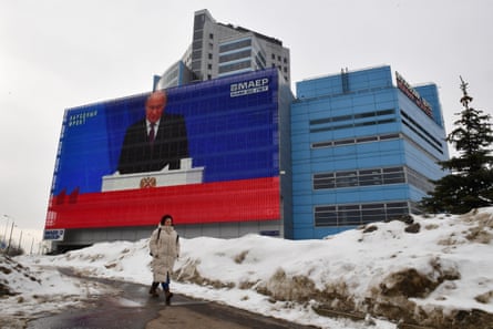 A woman walks past a screen displaying a broadcast of Putin’s annual state of the nation address.