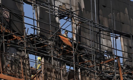 A firefighter seen through the window opening of a burnt-out building facade held up by scaffolding