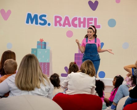 person wearing pink shirt and blue overalls sings in front of people