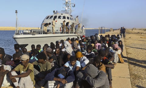 Rescued refugees and migrants sit next to a coastguard boat in Khoms, Libya, October 2019