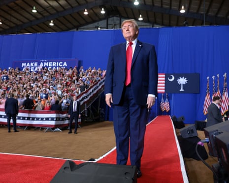 Donald Trump stands on a red carpet before a cheering crowd at a rally