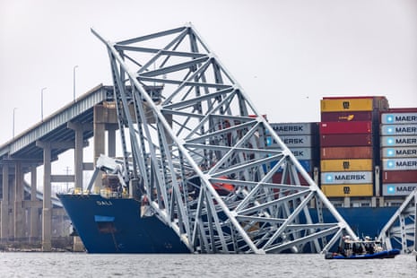 pieces of a giant metal structure rest on top of a blue ship stacked with colorful shipping containers
