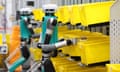 Two teal and gray, two-legged, two-armed robots appear to pull yellow plastic boxes off shelves.