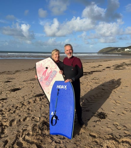 A middle-aged man and woman standing on a sandy beach holding surfboards