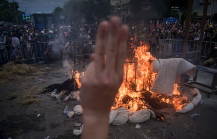 A protester makes a three-finger salute as they burn effigies signifying coronavirus victims.