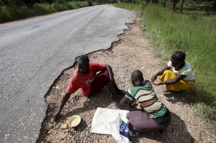 Women gather grain spilled by cargo trucks from Zambia along a highway in Magunje, Zimbabwe