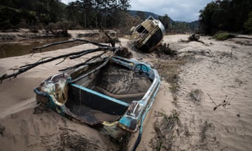 A yacht and its blue tender lay strewn on the banks of the MacDonald River, full of sand. A tree has fallen over the tender and vegetation is covered in mud after flooding