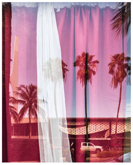 Palm trees and a flat-roofed building reflected in a window with closed red curtains