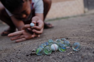 A child lines up a shot in a game of marbles on the dirt