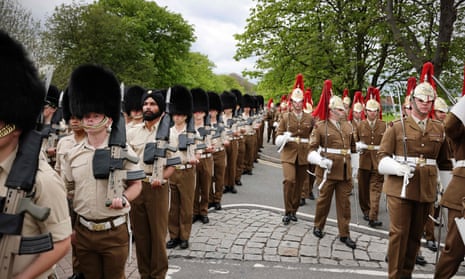 A parade of soldiers, some in full uniform, some in shirt sleeves with bearskins on their heads, on a march