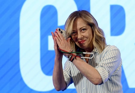 A smiling Giorgia Meloni presses her palms together as she raises her hands