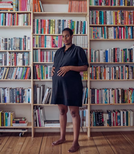 Sharmaine Lovegrove standing in front of floor-to-ceiling bookshelves, wearing a black dress and heavily pregnant