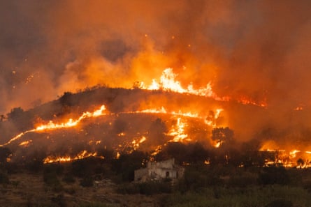Flames and smoke spreading across several tiered hillsides as seen at night