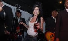 Amy Woinehoiuse smiling broadly and carrying a drink, walking in between other musicians onstage