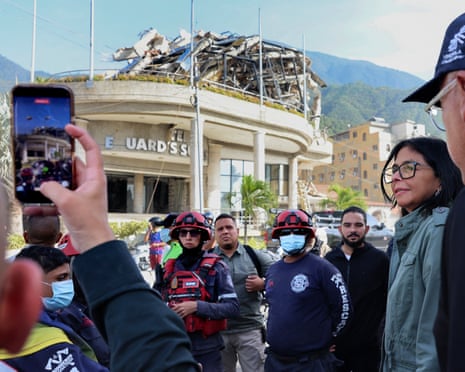 Delcy Rodriguez is seen with people gathered in front of a damaged building with collapsed roof debris, some filming on phones