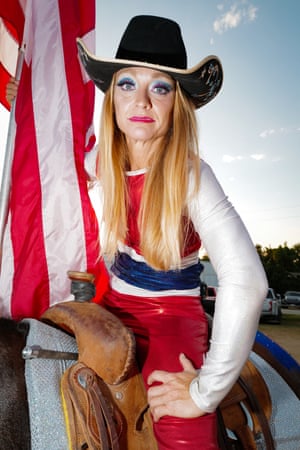 A heavily made up woman in a cowboy hat, wearing red white and blue, sits astride a horse