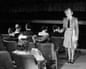 An usherette in a theatre aisle with a few people in the front row