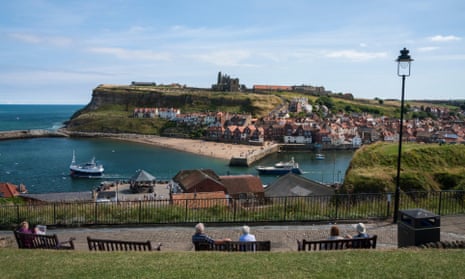 People sitting on benches look out over the harbour at Whitby