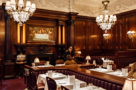 The traditional dark wood-panelled dining room at Simpson’s in the Strand, with tables laid with white tablecloths and low lighting.